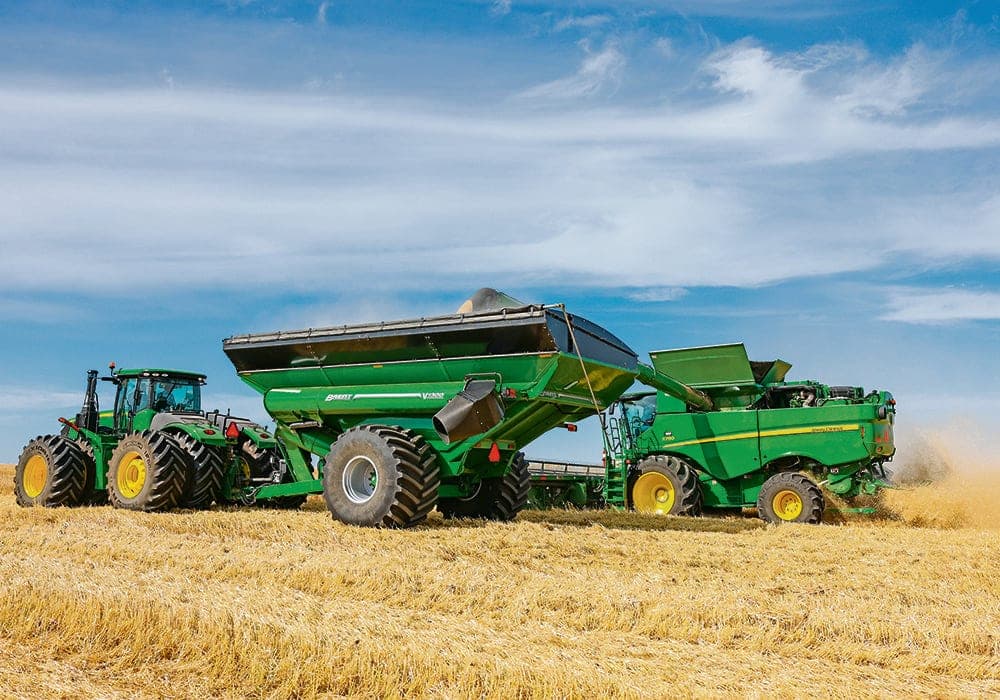 A combine unloading into a grain cart on the go in a cut wheat field